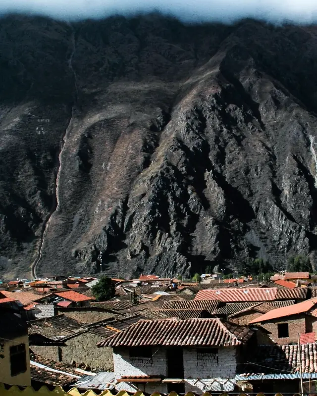 Terracotta roofs of a town sitting under a steep, shadowed mountain