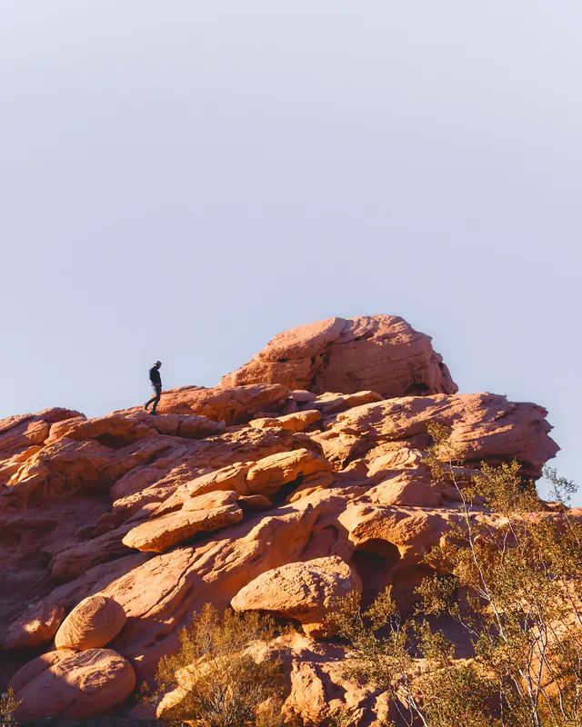 A person walking across sunlit red sandstone boulders