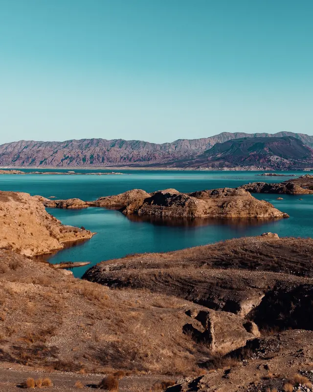 Turquoise water winding between brown rock islands, with layered mountains on the horizon